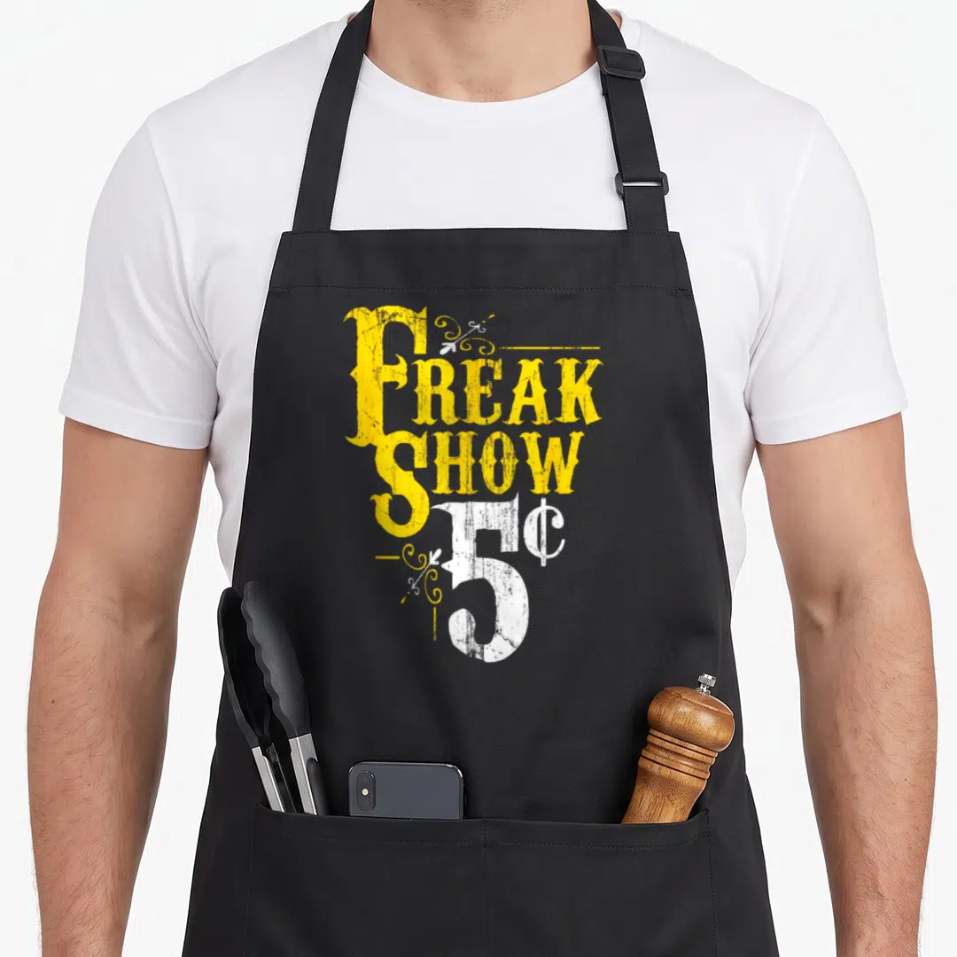 Show weird aprons - Distressed yellow and white text reading Freak Show 5c with decorative swirls — shown on a black cotton canvas apron against a white background