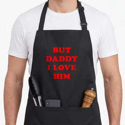 But daddy apron - Red stacked text reading BUT DADDY I LOVE HIM on grey background — shown on a black cotton canvas apron against a white background
