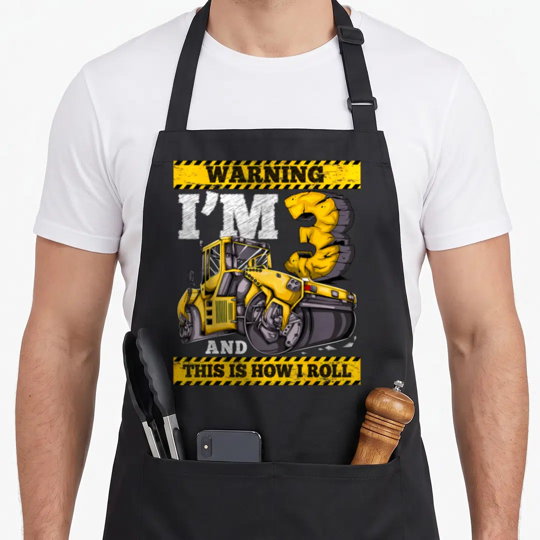 Roller construction apron - Yellow road roller graphic with warning stripes and I'M 3 text — shown on a black cotton canvas apron against a white background