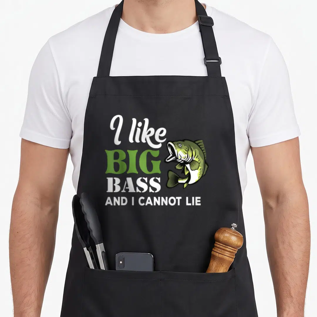 Cannot fishing aprons - Cartoon bass fish next to stacked text 'I like big bass and I cannot lie' in green and white — shown on a black cotton canvas apron against a white background