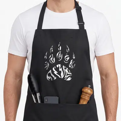 Paw native american apron - White paw print with flame negative space line art design — shown on a black cotton canvas apron against a white background