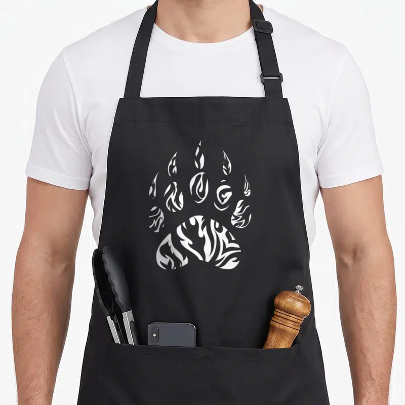 Paw native american apron - White paw print with flame negative space line art design — shown on a black cotton canvas apron against a white background