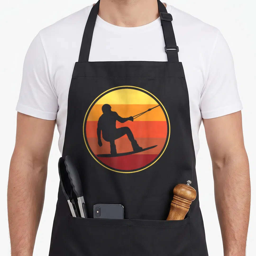 Wakeboarder wakeboarding life apron - Grey wakeboarder silhouette on striped yellow orange red sun circle — shown on a black cotton canvas apron against a white background