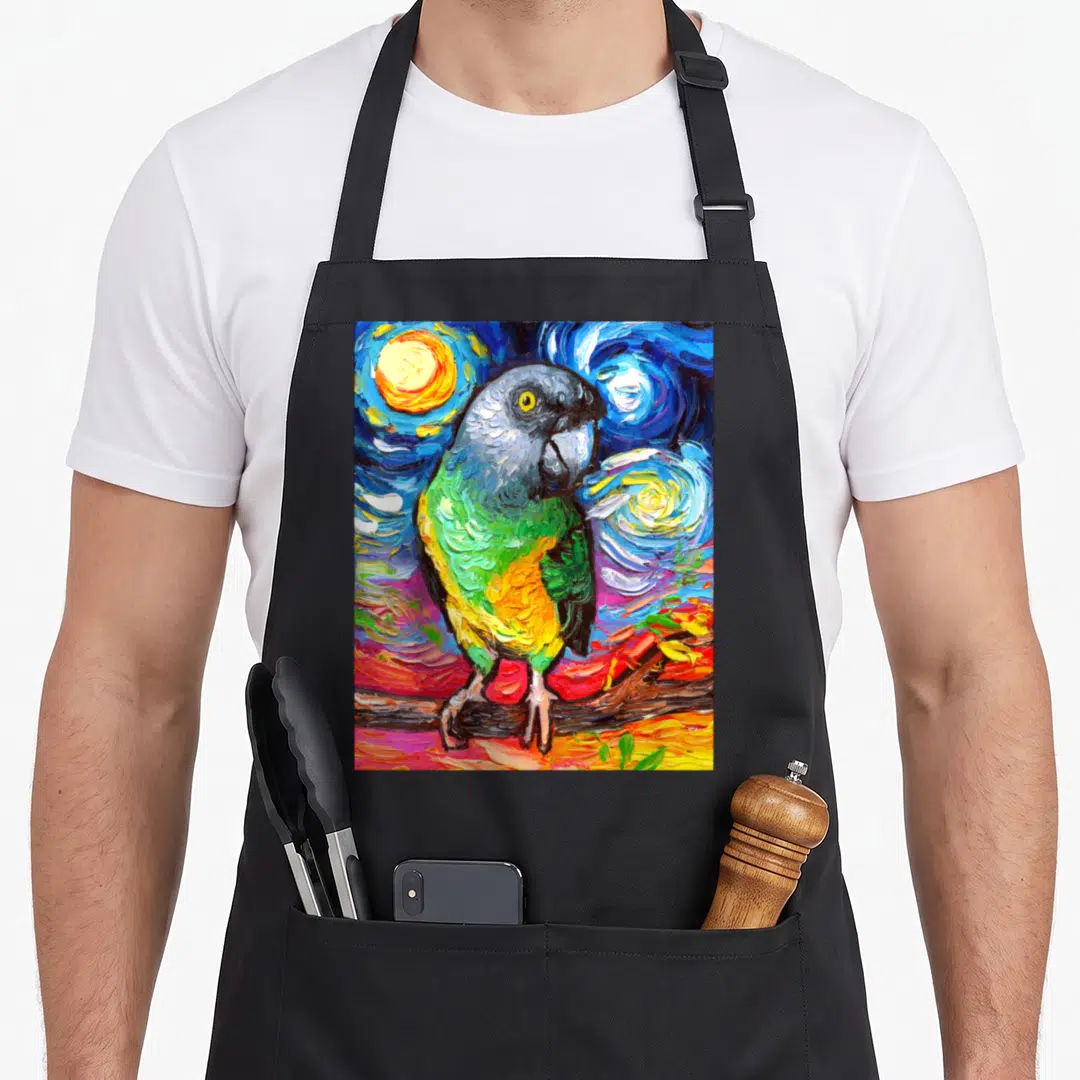 Aja bird apron - Watercolor parrot with blue green yellow red feathers on swirling starry night background — shown on a black cotton canvas apron against a white background