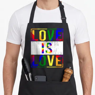 Csd gay pride apron - LOVE IS LOVE text in grey letters filled with red yellow green blue purple geometric rays — shown on a black cotton canvas apron against a white background