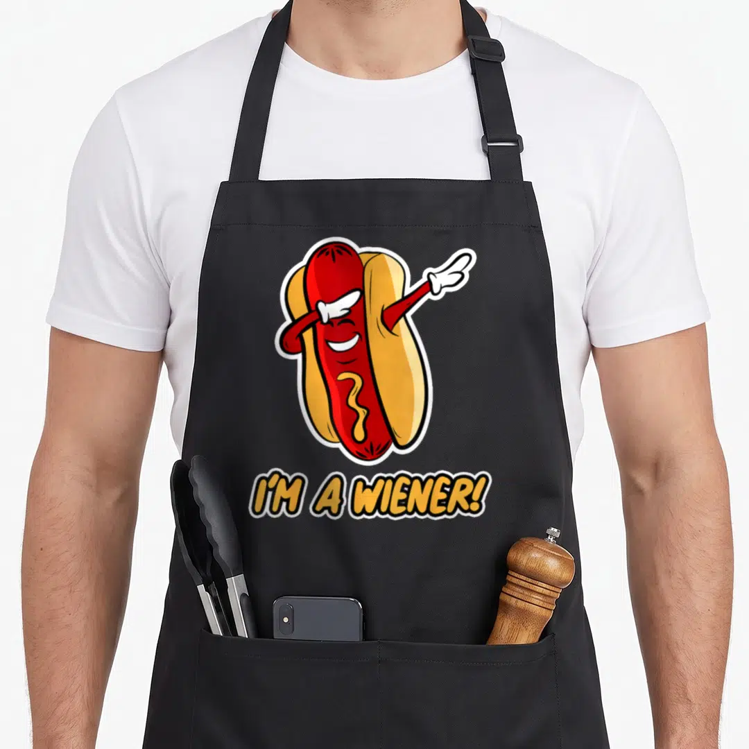 Hot dog wiener apron - Cartoon red hot dog with white gloves and yellow mustard above text I'M A WIENER! — shown on a black cotton canvas apron against a white background