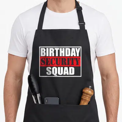 Security birthday apron - Stacked BIRTHDAY SECURITY SQUAD text in white and grey on red and grey backgrounds inside — shown on a black cotton canvas apron against a white background