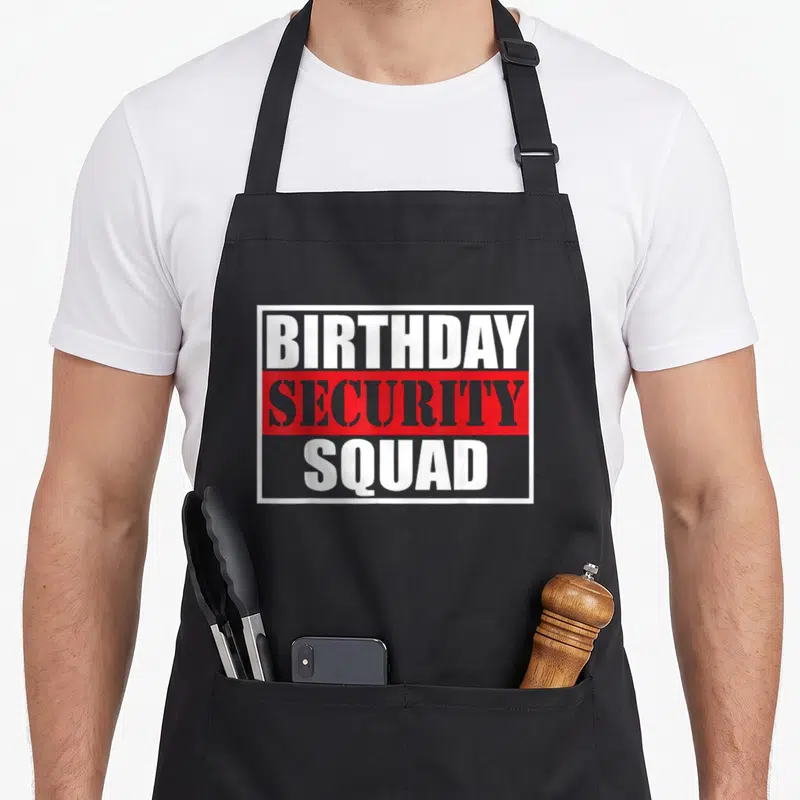 Security birthday apron - Stacked BIRTHDAY SECURITY SQUAD text in white and grey on red and grey backgrounds inside — shown on a black cotton canvas apron against a white background