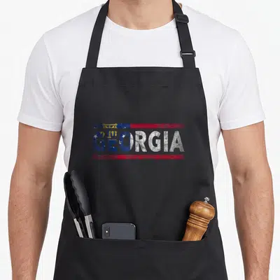 Georgia distressed apron - Stacked GEORGIA text filled with distressed blue red and white flag pattern — shown on a black cotton canvas apron against a white background