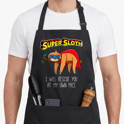 Hero sloth apron - Super Sloth text and masked sloth in red cape hanging from branch with rescue quote — shown on a black cotton canvas apron against a white background