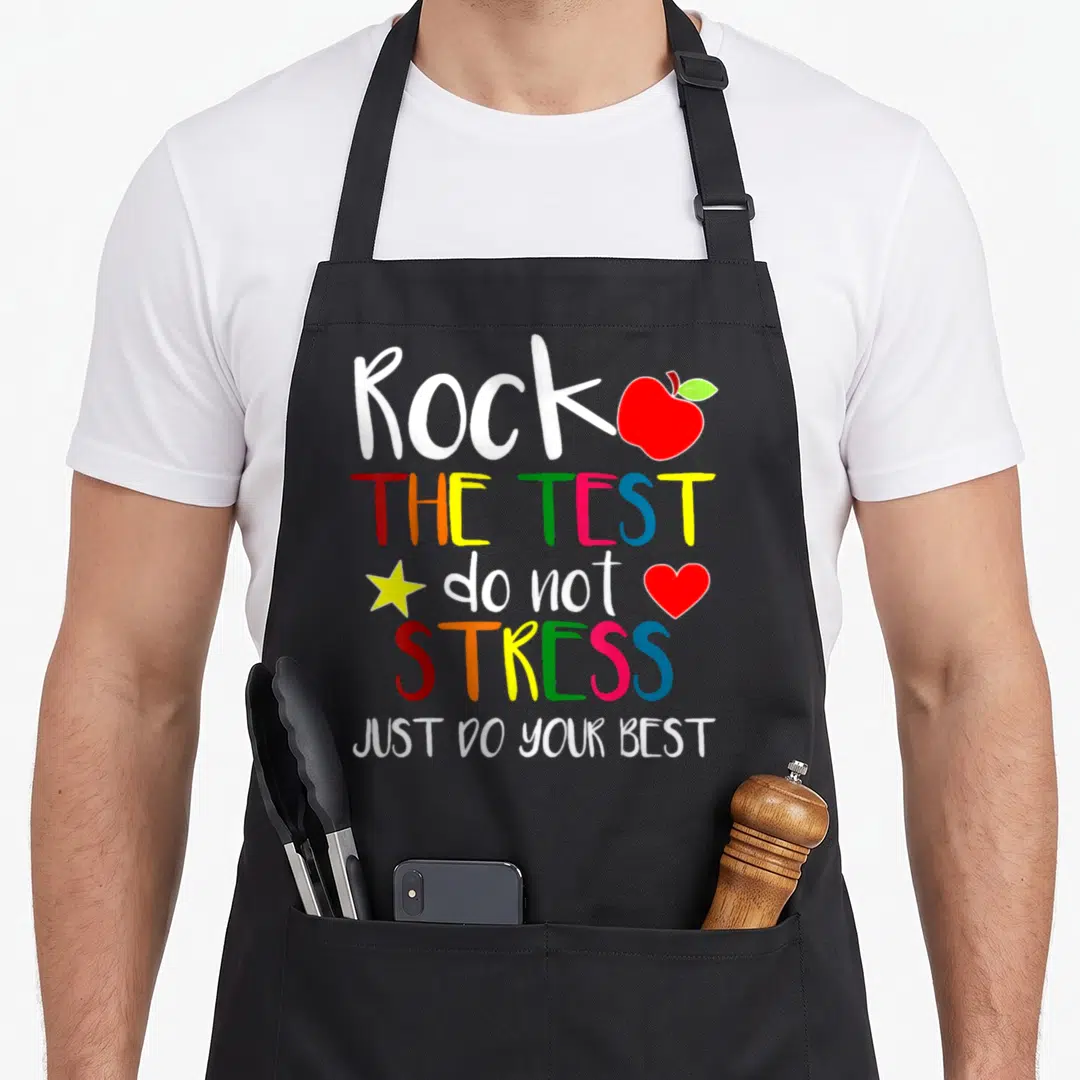 Rock test teacher apron - Stacked colorful text Rock The Test with red apple, yellow star, and heart icons — shown on a black cotton canvas apron against a white background