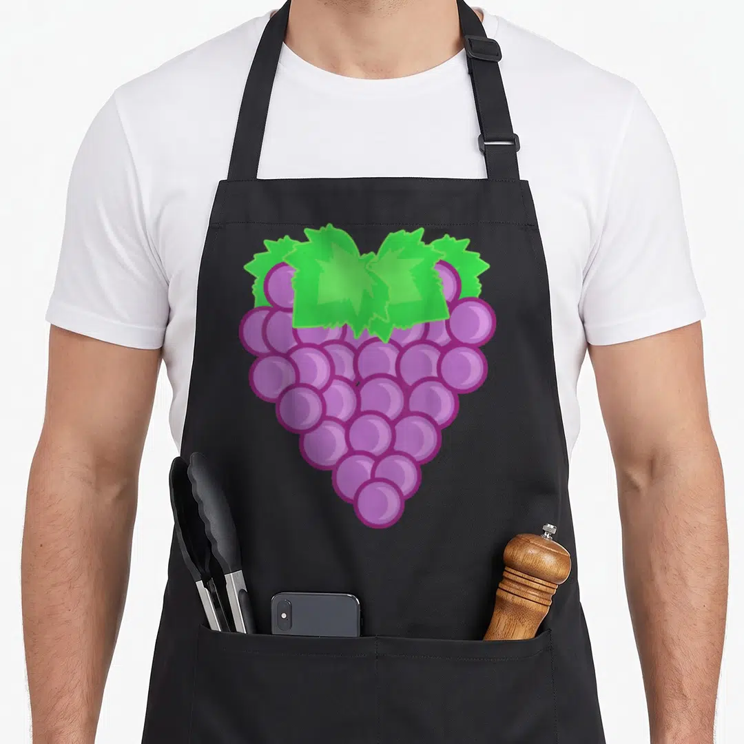 Grape fruit halloween apron - Cartoon purple grape cluster shaped like a heart with green leaves on black fabric — shown on a black cotton canvas apron against a white background