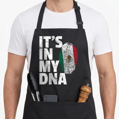 Dna mexican apron - Stacked IT'S IN MY DNA text beside a fingerprint filled with Mexican flag colors in white, green — shown on a black cotton canvas apron against a white background