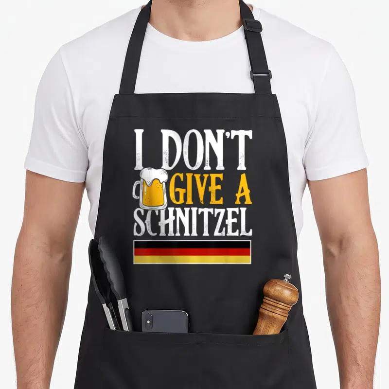 Give sausage apron - Beer mug next to text I DON'T GIVE A SCHNITZEL above German flag stripes — shown on a black cotton canvas apron against a white background