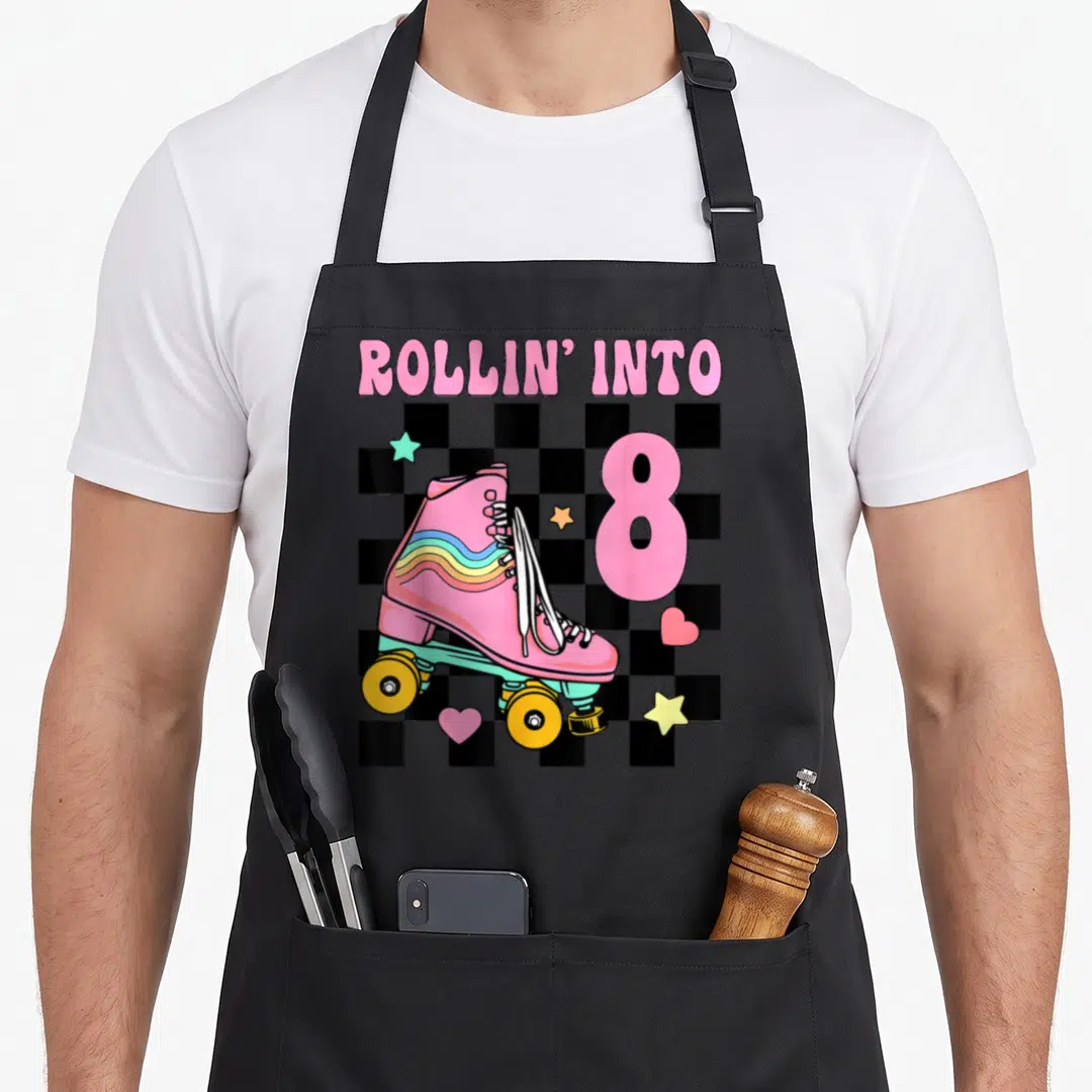 Rolling roller birthday apron - Pink roller skate, ROLLIN' INTO 8 text, checkerboard, stars, hearts — shown on a black cotton canvas apron against a white background