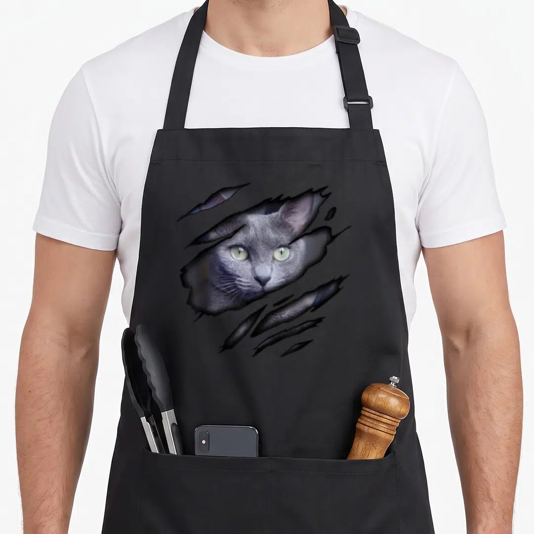 Blue russian aprons - Grey cat head emerging from torn grey surface with black shadow details — shown on a black cotton canvas apron against a white background