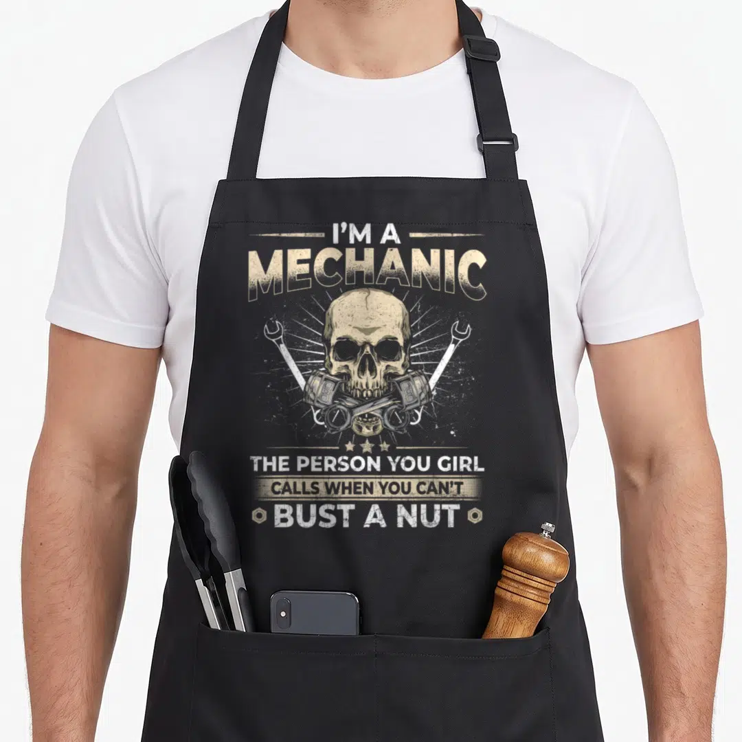 Vintage car auto mechanic apron - Tan distressed skull between crossed wrenches and pistons with five stars below — shown on a black cotton canvas apron against a white background