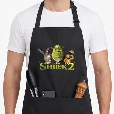 Donkey friends apron - Shrek Donkey Puss in Boots photo print with yellow SHREK 2 text below — shown on a black cotton canvas apron against a white background