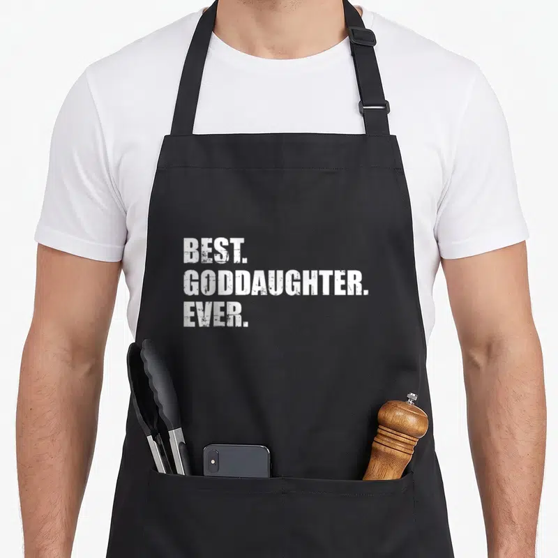 Goddaughter daughter of god apron - Stacked white text reading BEST GODDAUGHTER EVER on gray background — shown on a black cotton canvas apron against a white background