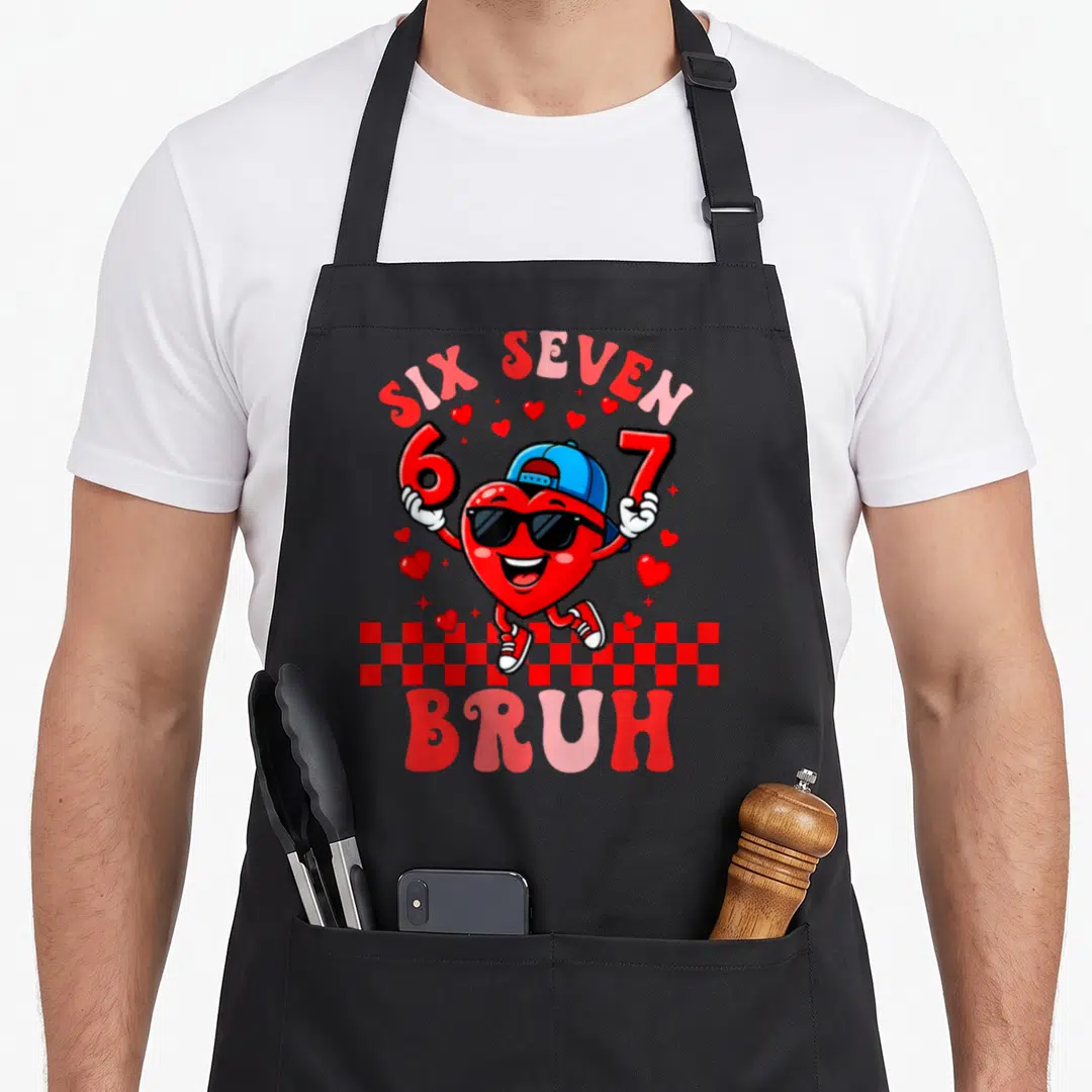 Six valentine apron - Cartoon heart holding six and seven with bruh text and checkerboard — shown on a black cotton canvas apron against a white background