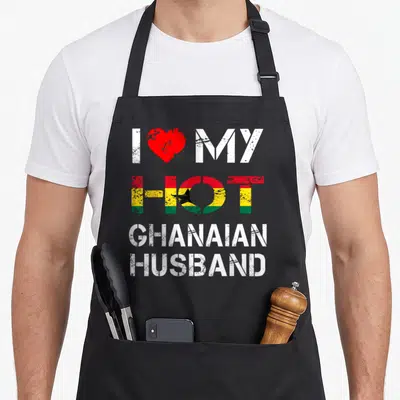 Ghanaian husband apron - Distressed text I MY HOT GHANAIAN HUSBAND with red heart and flag pattern fill — shown on a black cotton canvas apron against a white background