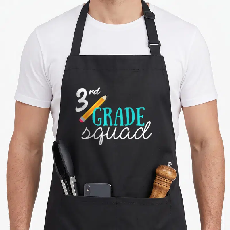 3rd art teacher aprons - 3rd GRADE squad text with diagonal yellow pencil and turquoise lettering in cartoon style — shown on a black cotton canvas apron against a white background