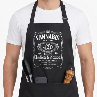 Cannabis tijuana apron - White vintage label print reading Cannabis High Time Old 420 Brand Indica Sativa — shown on a black cotton canvas apron against a white background