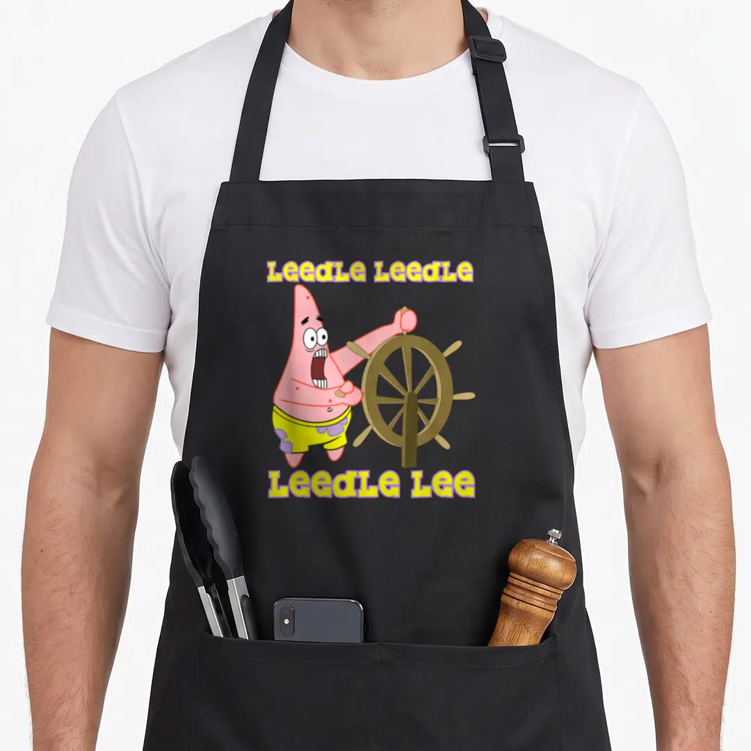Leedle patrick apron - Patrick Star holding brown ship wheel with yellow LeedLe text — shown on a black cotton canvas apron against a white background