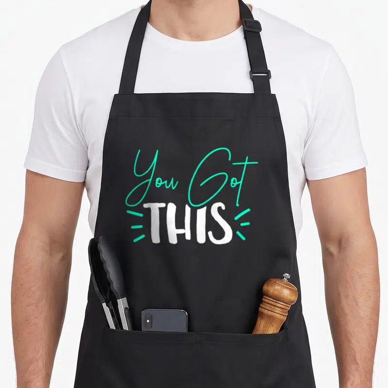 Funny teacher test kitchen apron - You Got THIS text design in turquoise script and white block font with three accent — shown on a black cotton canvas apron against a white background