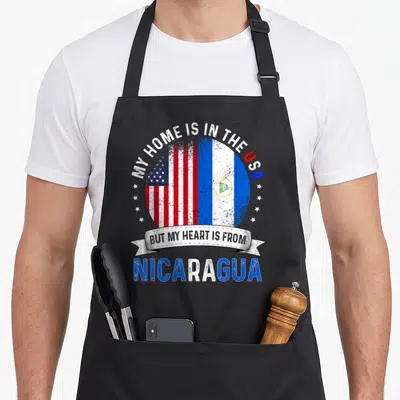 Nicaraguan patriot american flag apron - Distressed circular graphic with USA and Nicaragua flags flanked by small — shown on a black cotton canvas apron against a white background