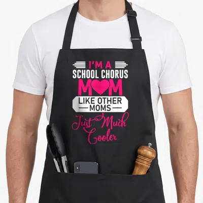 School mother's day aprons - Pink and white text reading I'm a School Chorus Mom with heart replacing O and banner — shown on a black cotton canvas apron against a white background