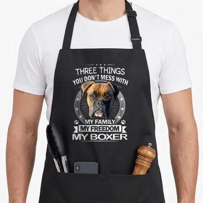 Three boxer dog apron - Realistic boxer head in circle with Three Things You Don't Mess With text — shown on a black cotton canvas apron against a white background