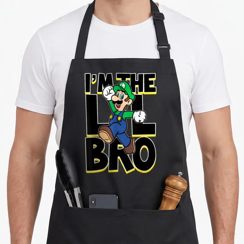 Lil bro holiday apron - Luigi leaping in front of stacked black text reading I'M THE LIL BRO with yellow outlines — shown on a black cotton canvas apron against a white background