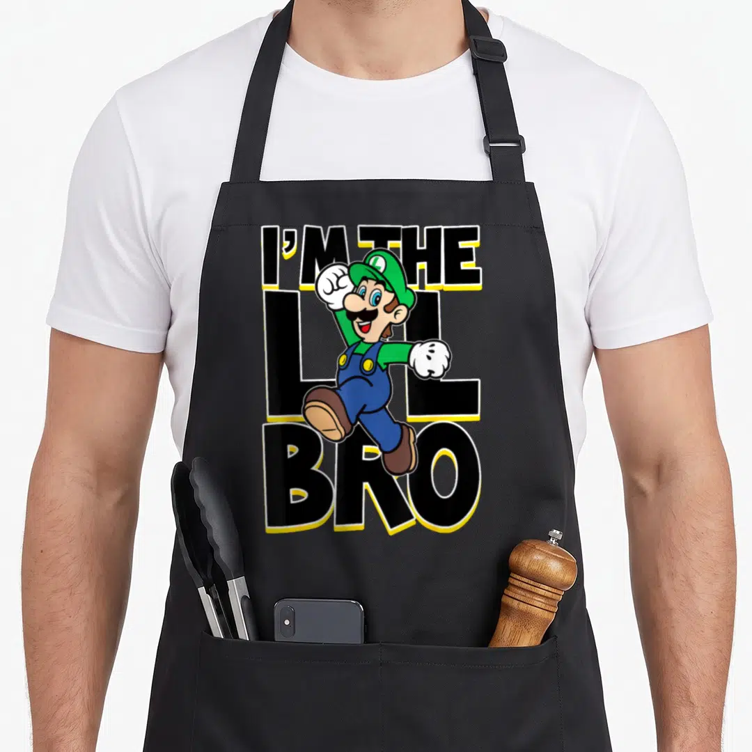 Lil bro holiday apron - Luigi leaping in front of stacked black text reading I'M THE LIL BRO with yellow outlines — shown on a black cotton canvas apron against a white background