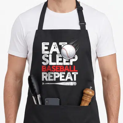 Repeat catcher baseball apron - Stacked EAT SLEEP BASEBALL REPEAT text with white ball and bat in white and red — shown on a black cotton canvas apron against a white background
