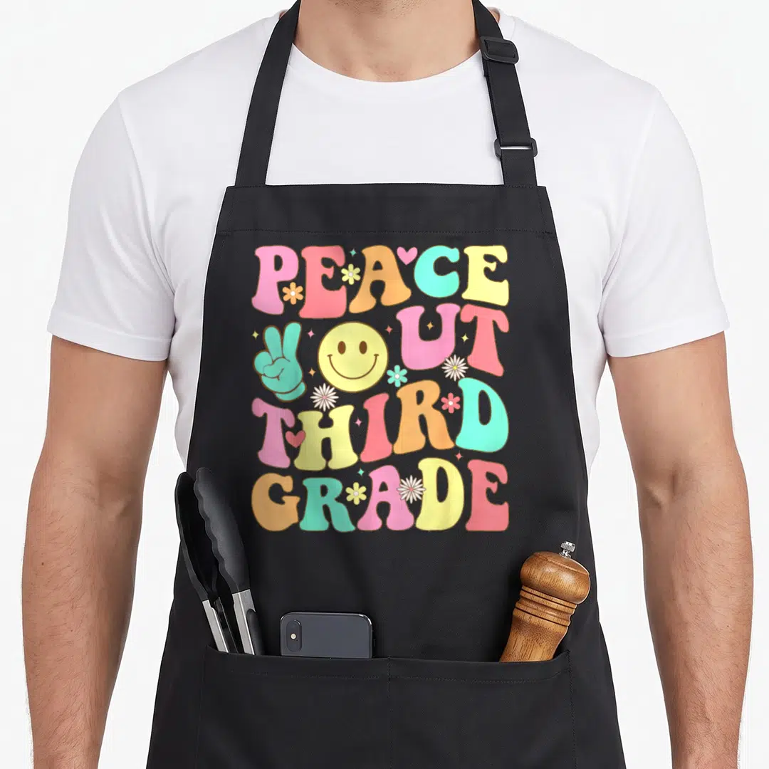 Peace third groovy grade apron - Retro text reading PEACE OUT THIRD GRADE with smiley face and teal peace sign hand — shown on a black cotton canvas apron against a white background