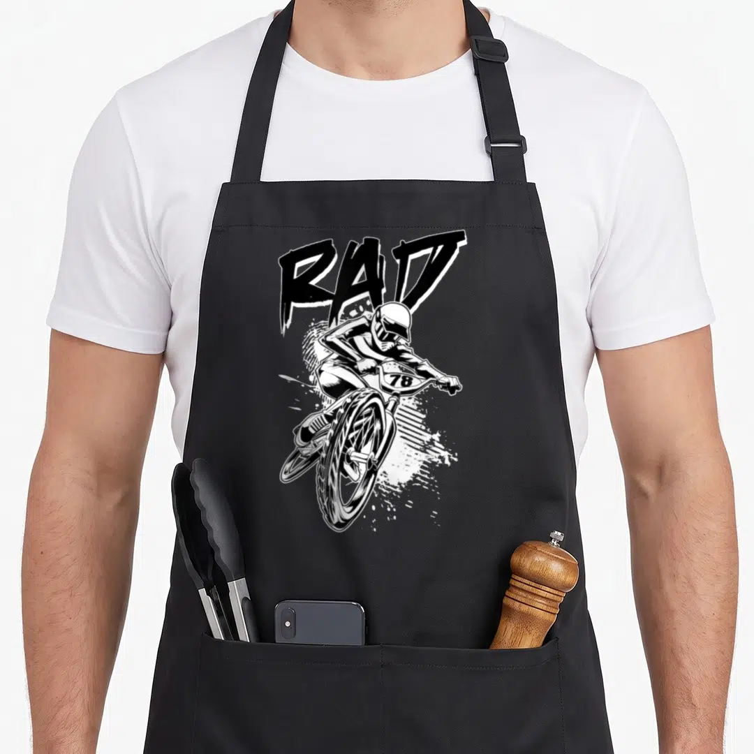 Rad bmx apron - RAD text above helmeted cyclist wheelie with 78 plate, black and white splatter line art — shown on a black cotton canvas apron against a white background