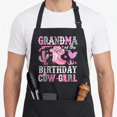 Grandma birthday cowgirl aprons - Pink cowgirl boots hat gun and cacti with GRANDMA BIRTHDAY COW-GIRL text — shown on a black cotton canvas apron against a white background