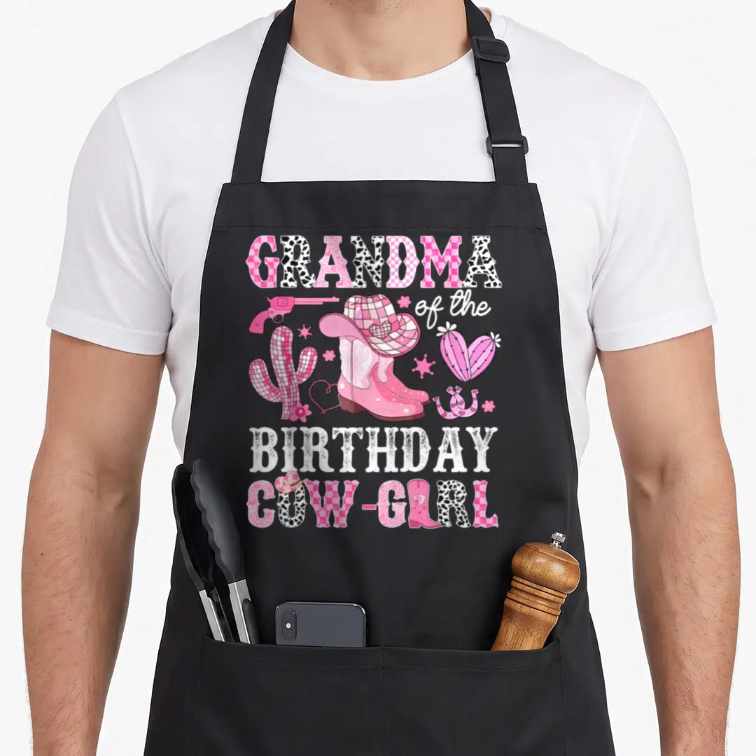 Grandma birthday cowgirl aprons - Pink cowgirl boots hat gun and cacti with GRANDMA BIRTHDAY COW-GIRL text — shown on a black cotton canvas apron against a white background