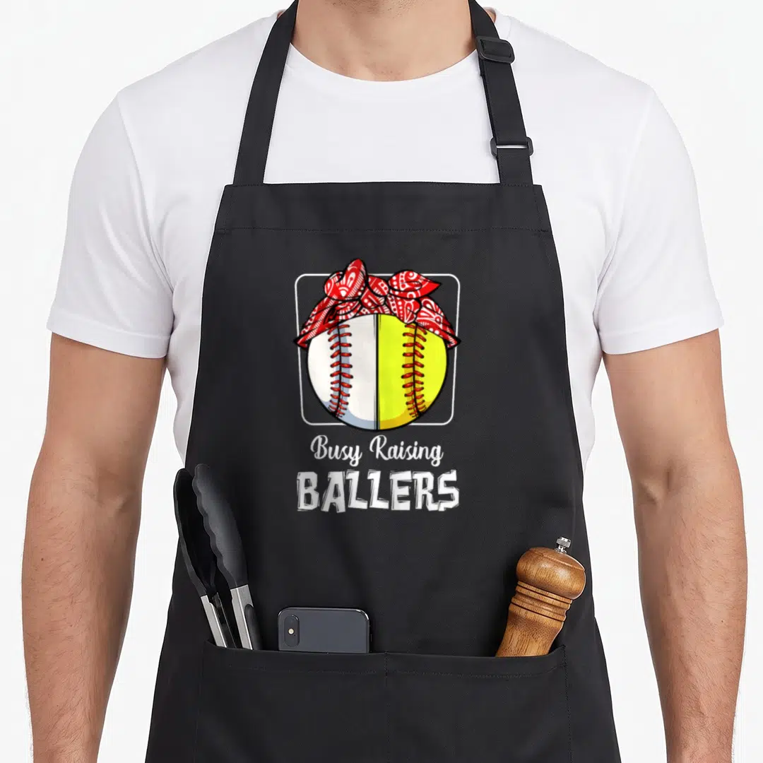 Softball busy apron - Split baseball with red bandana and Busy Raising Ballers text — shown on a black cotton canvas apron against a white background
