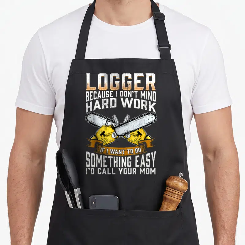 Logger woodworker's apron - Crossed yellow chainsaws with white text and orange banner reading logger hard work — shown on a black cotton canvas apron against a white background