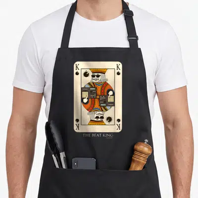 Beatmaker king apron - Mirrored playing card king with sunglasses operating a mixing console surrounded by four K — shown on a black cotton canvas apron against a white background