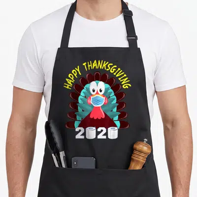 Face thanksgiving apron - Cartoon turkey in blue mask with HAPPY THANKSGIVING text and 2020 toilet paper zeros — shown on a black cotton canvas apron against a white background