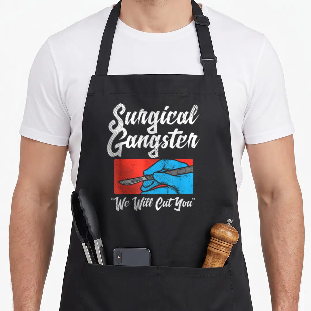 Tech surgeon apron - Surgical Gangster text, blue hand holding scalpel on red background, We Will Cut You quote — shown on a black cotton canvas apron against a white background