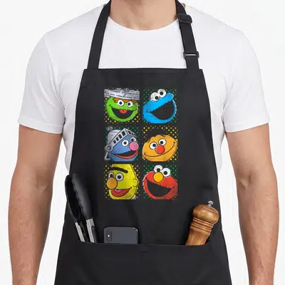 Cute square apron - Six muppet character heads in a grid on polka dot backgrounds in green blue orange yellow and red — shown on a black cotton canvas apron against a white background