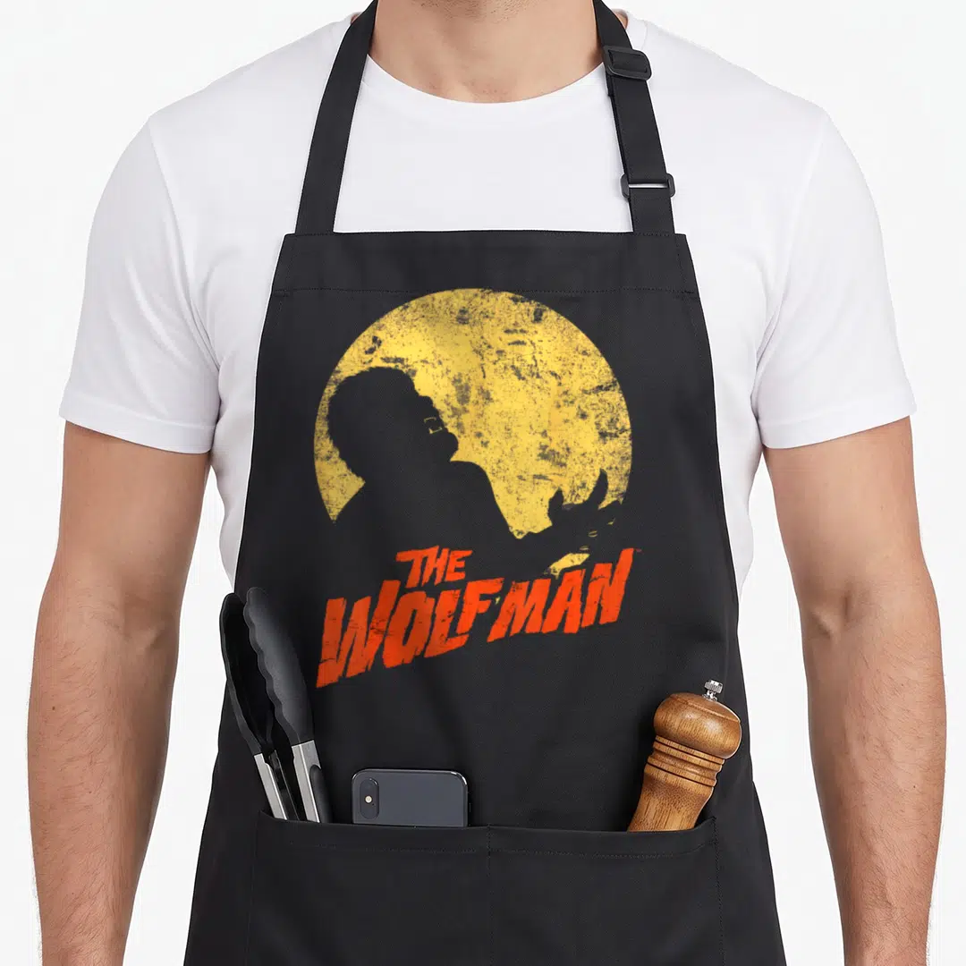 Wolf ogre apron - Black werewolf silhouette against yellow moon with red distressed THE WOLFMAN text — shown on a black cotton canvas apron against a white background