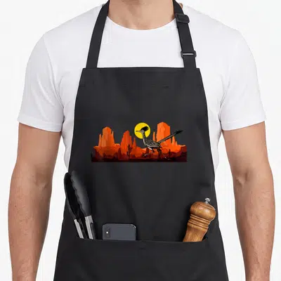 Roadrunner mexico apron - Minimalist roadrunner running left past orange rocks and yellow sun in desert landscape — shown on a black cotton canvas apron against a white background