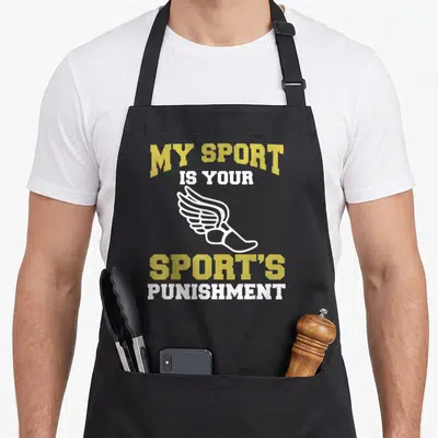 Sport track apron - Gold and white text MY SPORT IS YOUR SPORT'S PUNISHMENT with a white winged shoe icon — shown on a black cotton canvas apron against a white background