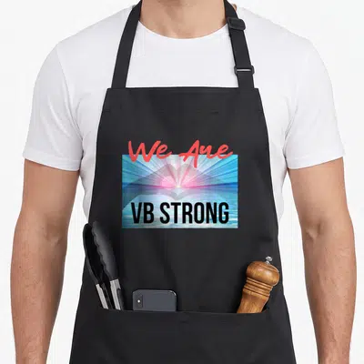 Virginia strong man apron - We Are VB STRONG red script over blue pink sunrise heart photo with black block letters — shown on a black cotton canvas apron against a white background