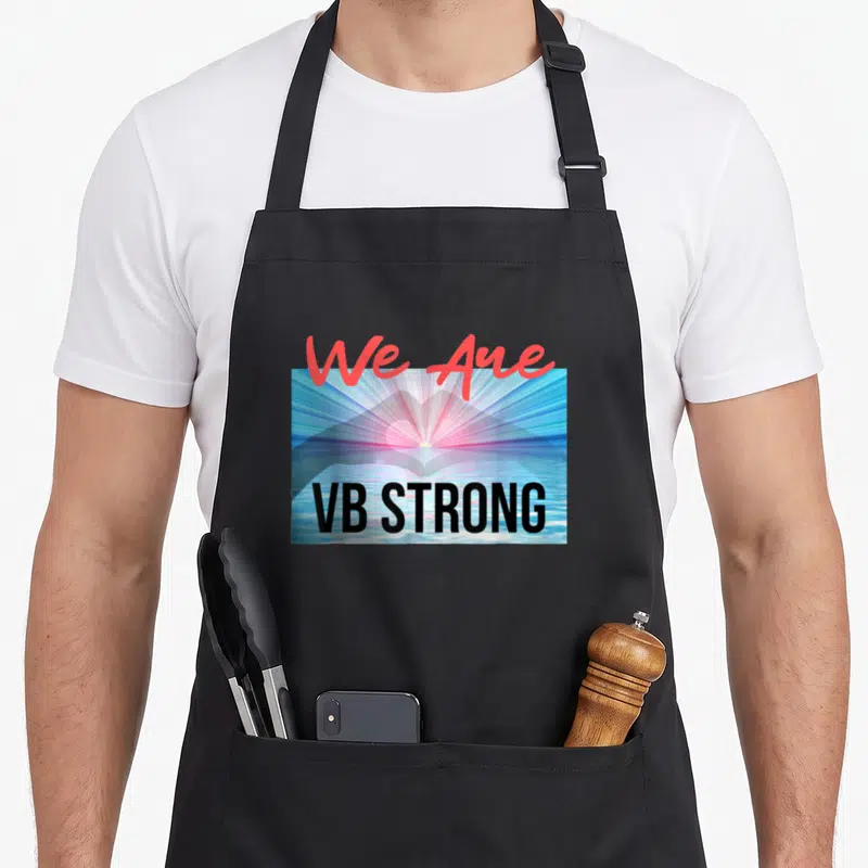 Virginia strong man apron - We Are VB STRONG red script over blue pink sunrise heart photo with black block letters — shown on a black cotton canvas apron against a white background